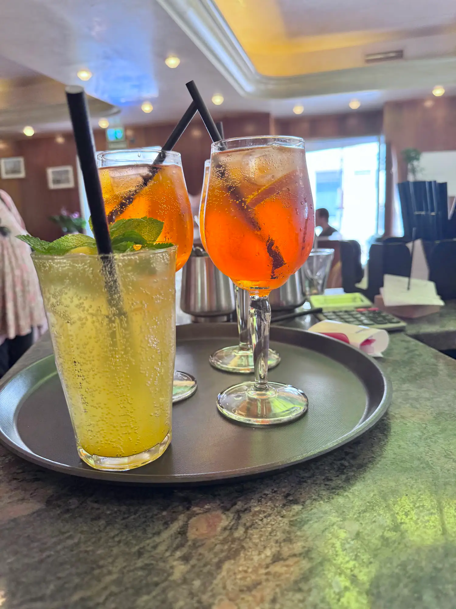 Drei bunte Kaltgetränke, darunter orange Spritzer, auf einem Serviertablett an der Bar