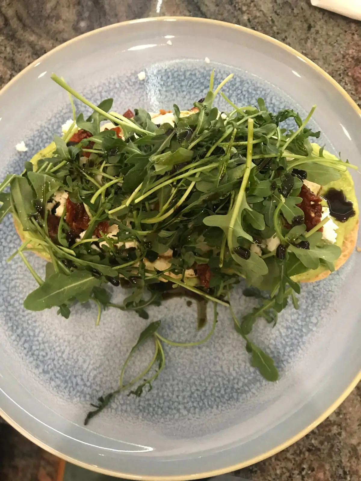 Avocado-Toast mit Ziegenkäse, getrockneten Tomaten und Rucola auf hellblauem Teller