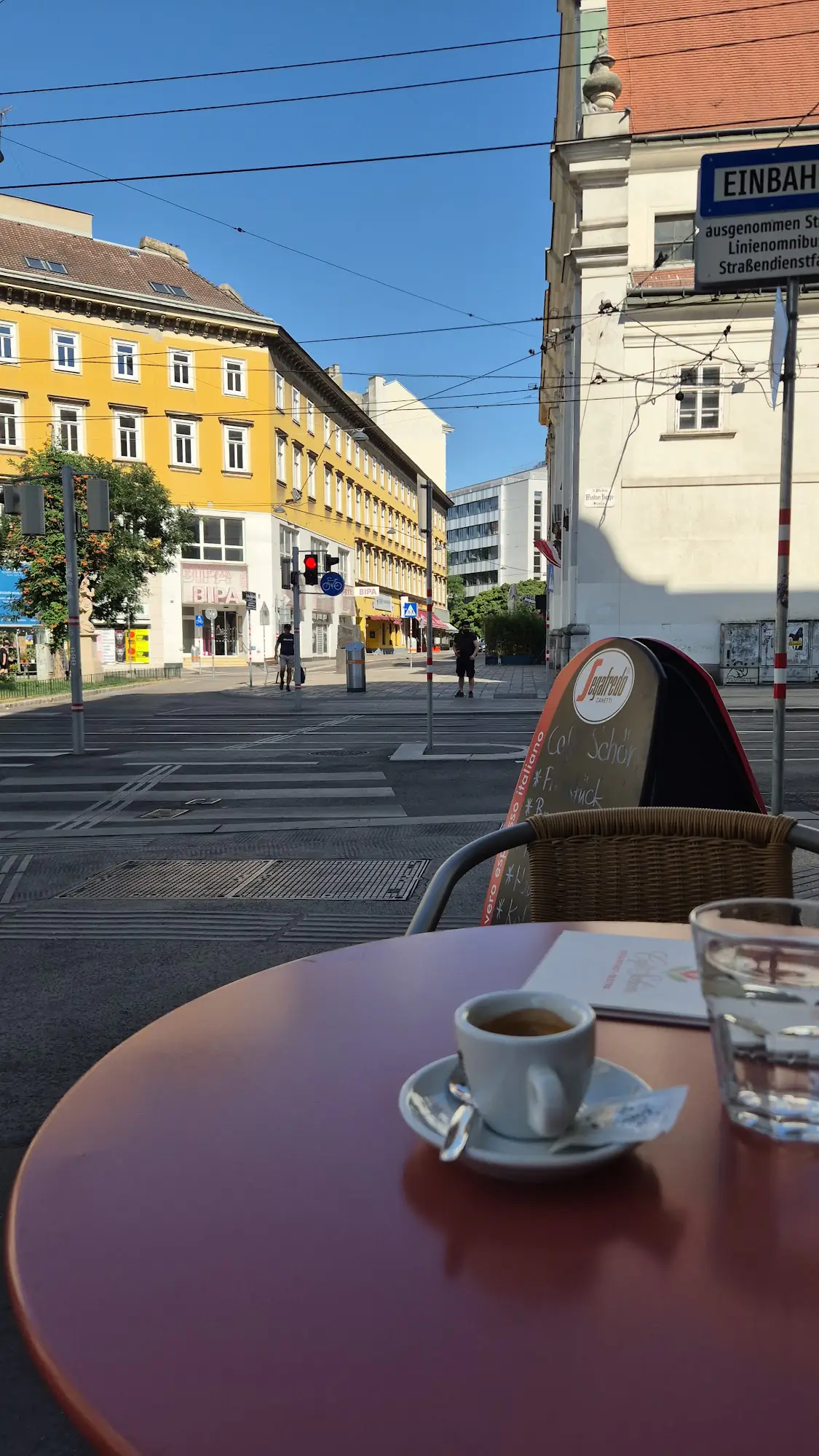 Espresso und Wasserglas auf einem Tisch vor dem Café mit Blick in die sonnige Gasse