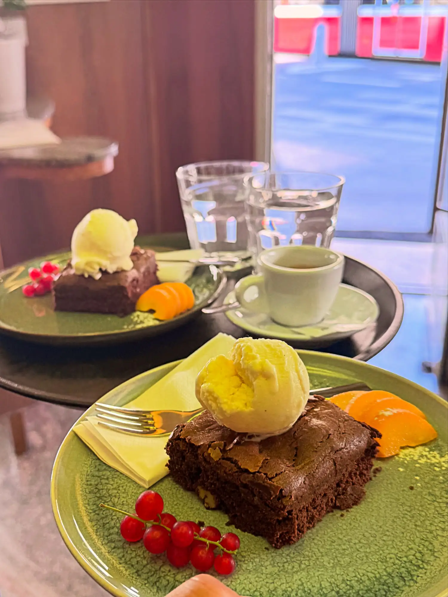 Brownies mit Vanilleeis, Ribiseln und Orangenscheiben auf grünen Keramiktellern