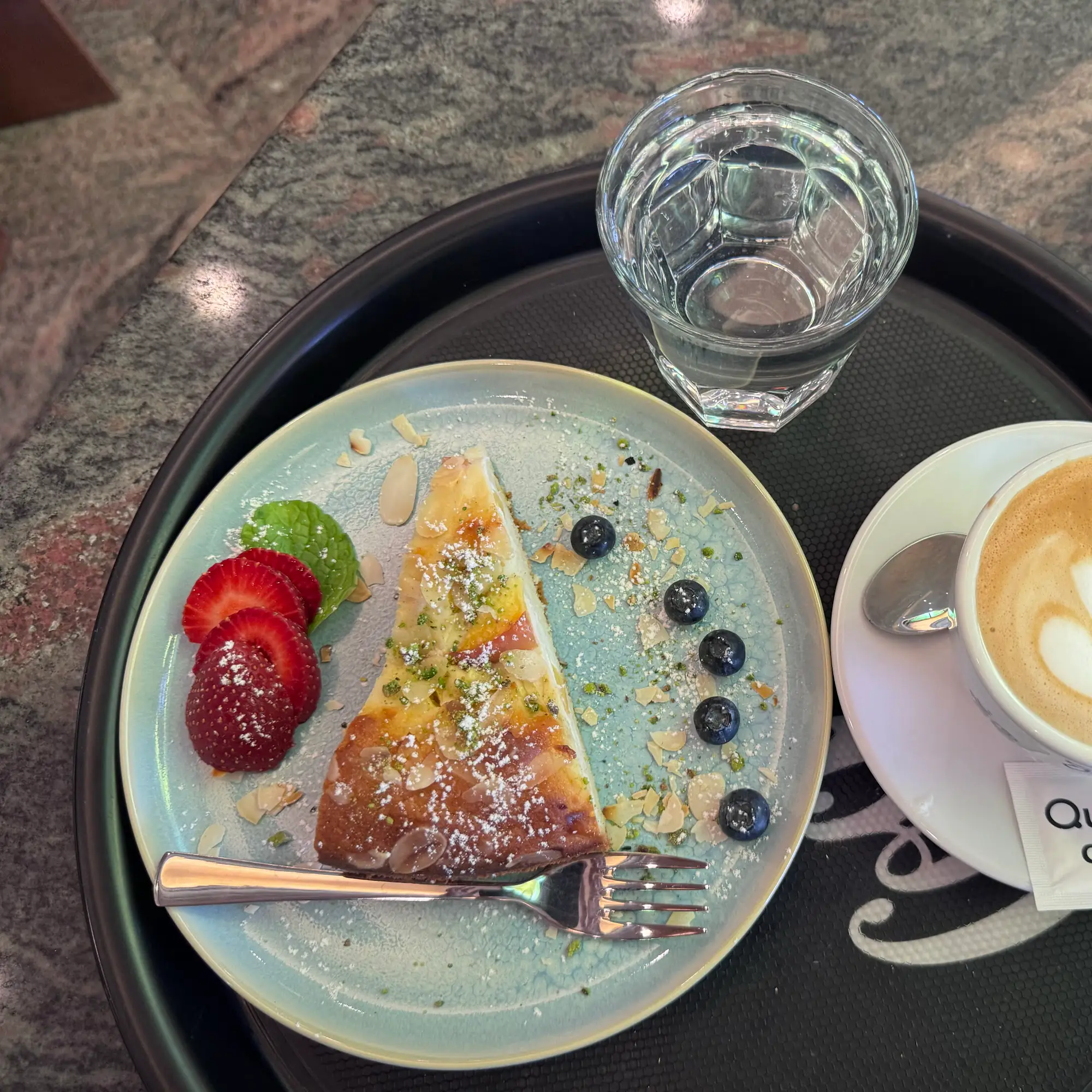 Cheesecake mit Beeren und Mandelblättchen, serviert mit Kaffee und Wasserglas